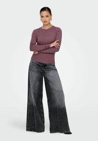 Maglietta viola a maniche lunghe abbinata a jeans in denim neri a gamba larga, con effetto sfumato e una sottile trama sbiadita.