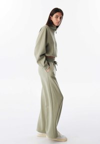 Lichtgroene cropped sweatshirt met hoge kraag en rits, gecombineerd met bijpassende wijde sweatpants met elastische tailleband en zakken.