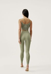 Olive green ribbed fitness outfit featuring a cropped top with cross-back straps and high-waisted leggings with a zigzag pattern.
