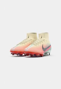 Nike nogometne kopačke s kremastim pletenim gornjim dijelom, gradijent dizajn u ružičastoj do narančastoj boji, crni swoosh i prozirna potplata u crvenoj i plavoj boji.