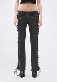 Σκούρα γκρι τζιν παντελόνια με κανονική γραμμή, με λεπτομέρειες κορδονιών στο πλάι και φερμουάρ μπροστά. Φοράγονται με μαύρα μποτάκια αστραγάλου.