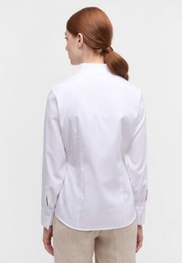 White long-sleeve shirt featuring a mock collar, textured fabric, and buttoned cuffs. Shaped for a tailored fit with a curved hem.