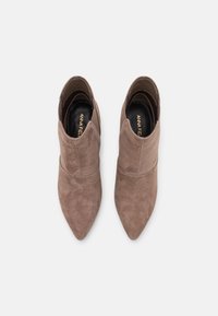 Stivaletti con punta appuntita in camoscio marrone chiaro con una texture liscia e un design minimalista, caratterizzati da cuciture discrete e una morbida fodera interna.