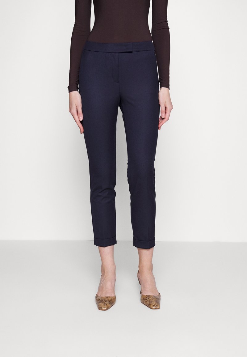 Navy skinny trousers met een platte voorkant, opgerolde broekspijpen en een gladde textuur, gecombineerd met beige pumps met een spitse neus in een slangenprint.