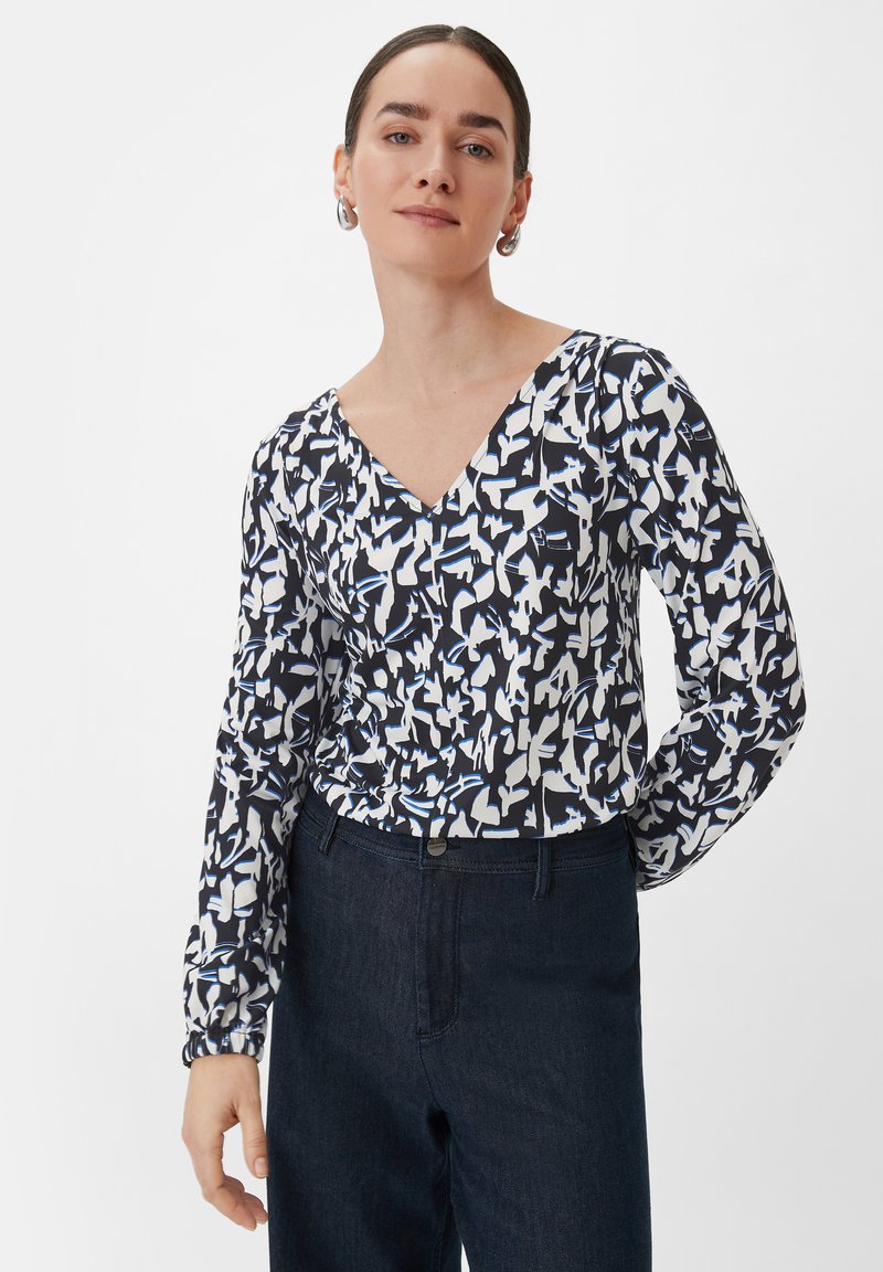 Langsleeve blouse in een marineblauw en wit abstract patroon, met een V-hals en elastische manchetten, gecombineerd met donkere denim jeans.