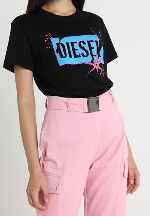 Persona que lleva una camiseta negra con el logo de Diesel, decorada con un gráfico en azul y rosa, y pantalones cargo de tiro alto en rosa claro con un cinturón ancho.