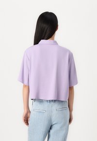 Kuttet kortermet skjorte i lys lavendelstoff med krage. Glatt tekstur og løs passform, kombinert med lyseblå høytlivsjeans.