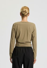 Haut à manches longues de couleur marron clair, présentant une coupe ajustée avec un col rond et une taille froncée, associé à un pantalon noir à taille élastique.