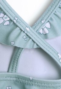 Top bikini a stampa floreale verde menta con bordi arricciati e spalline incrociate. Materiale morbido con una texture liscia e cuciture a contrasto.
