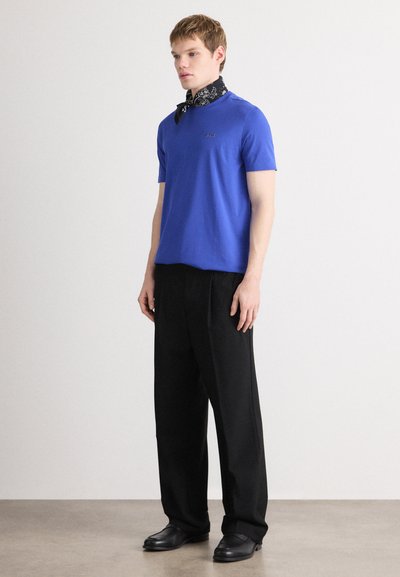 T-shirt bleu à manches courtes avec logo, associé à un pantalon noir à jambes larges et un foulard de cou noir à motif. Tissu doux et coupe décontractée.