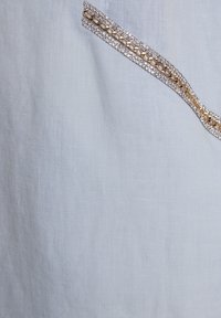 Lichtblauwe linnen stof heeft een decoratieve rand van heldere rhinestones en een gouden ketting langs de rand, wat textuur en detail toevoegt.