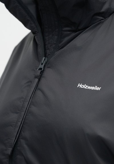 Μαύρο μπουφάν με φερμουάρ και κουκούλα, που δείχνει το εμπρόσθιο φερμουάρ και το λευκό λογότυπο Holzweiler στο στήθος.