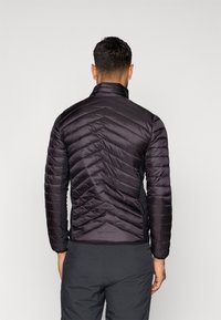 Melnā pūkainā jaka ar diagonālu quilted rakstu, augstu apkakli un pieguļošu dizainu. Gluda tekstūra un viegla uzbūve.