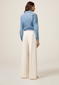 Lichtblauwe denim shirt met knopenmanchetten en detail op de rug, in combinatie met crèmekleurige wijde broek met elastische tailleband.