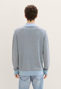 Sweter z dzianiny w jasnoniebieskim kolorze, z poziomymi paskami w ciemniejszym odcieniu niebieskiego. Posiada ribbowany kołnierz i mankiety; tkanina o fakturze.