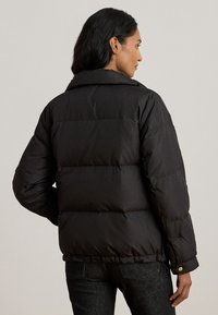 Μαύρο μπουφάν τύπου puffer με ψηλό γιακά, μονωμένο σχέδιο και ορατές ραμμένες τμήματα. Διαθέτει μανσέτες με κουμπιά και ίσια γραμμή στο τελείωμα.