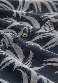 Marinefarbener Stoff mit einem weißen Blättermuster und einer strukturierten Oberfläche. Braune Knöpfe betonen das Design in der Nähe des Stoffansatzes.