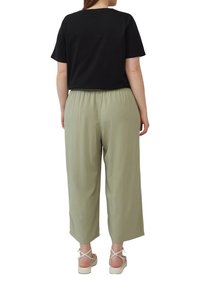 T-shirt noire à manches courtes associée à un pantalon large de couleur vert olive clair. Le pantalon présente une taille élastique, une texture lisse et une coupe décontractée.