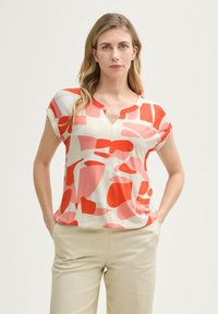 Blouse à manches courtes avec un col en V, fabriquée en tissu léger, ornée d'un motif abstrait de formes rouges, roses et crème.