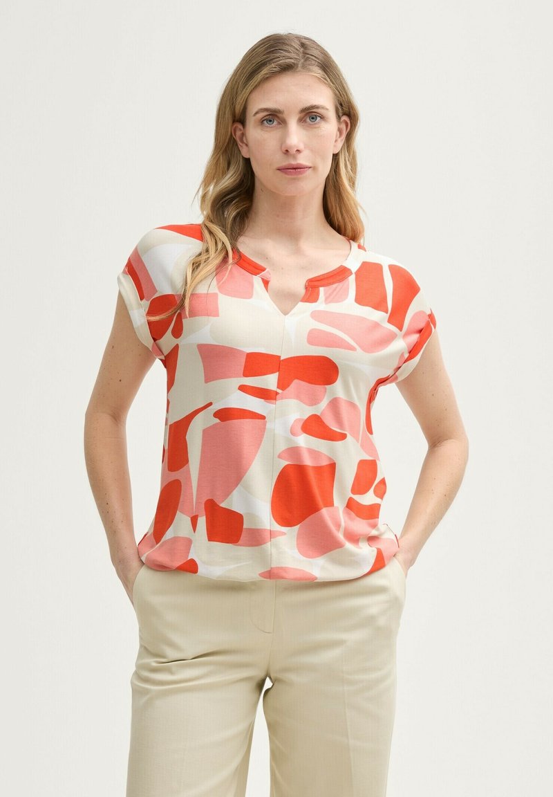 Blouse à manches courtes avec un col en V, fabriquée en tissu léger, ornée d'un motif abstrait de formes rouges, roses et crème.