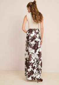 Jupe longue et fluide avec un imprimé vache brun et blanc, en satin, associée à un haut beige ajusté, mettant en valeur une texture lisse et un éclat.