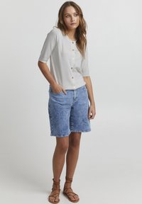 Lys grå kortærmet cardigan med rund halsudskæring og knaplukning, parret med lyseblå denim shorts og brune remsandaler.