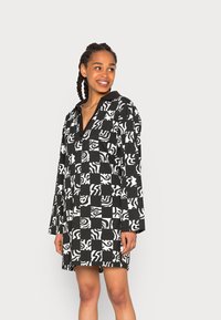 Vestido preto e branco com padrão, de mangas longas, colarinho e um corte solto. O design apresenta formas abstratas e espirais alternadas.
