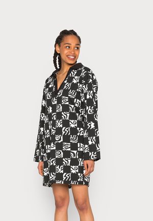 Vestido preto e branco com padrão, de mangas longas, colarinho e um corte solto. O design apresenta formas abstratas e espirais alternadas.