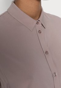 Košile s krátkým rukávem v světlém mauve odstínu, s špičatým límcem, čtyřmi knoflíky, hladkou texturou a slim fit střihem.