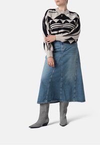 Sweter z dzianiny w geometryczne wzory w kolorze kremowym i granatowym, połączony z jasnoniebieską długą spódnicą dżinsową oraz szarymi, wysokimi na kolano, spiczastymi botkami.