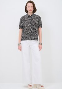 Camicia a maniche corte bianca e nera con colletto, abbinata a pantaloni bianchi a gamba larga e scarpe platform chunky.