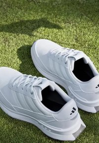 White athletic shoes with a textured upper, round toe, and three stripe accents on the sides. Treaded soles and cushioned heels are visible.