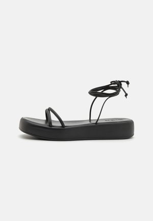 Mustad mustad sandaalid laia tallaga, õhukeste rihmadega ja reguleeritava sidumisega pahkluu ümber. Sile tekstuur ja minimalistik disain.