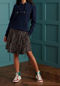 Sudadera de marina con bolsillo frontal y cordón; falda con estampado floral; zapatillas blancas de caña alta con acentos en rojo y azul verdoso.