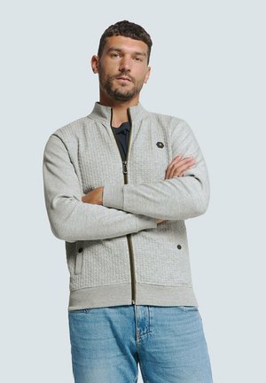 Lichtgrijze zip-up jas met textuurpanelen, zwarte hardware-accenten en geribde boorden. Draag over een donkere top en gecombineerd met lichte denim jeans.