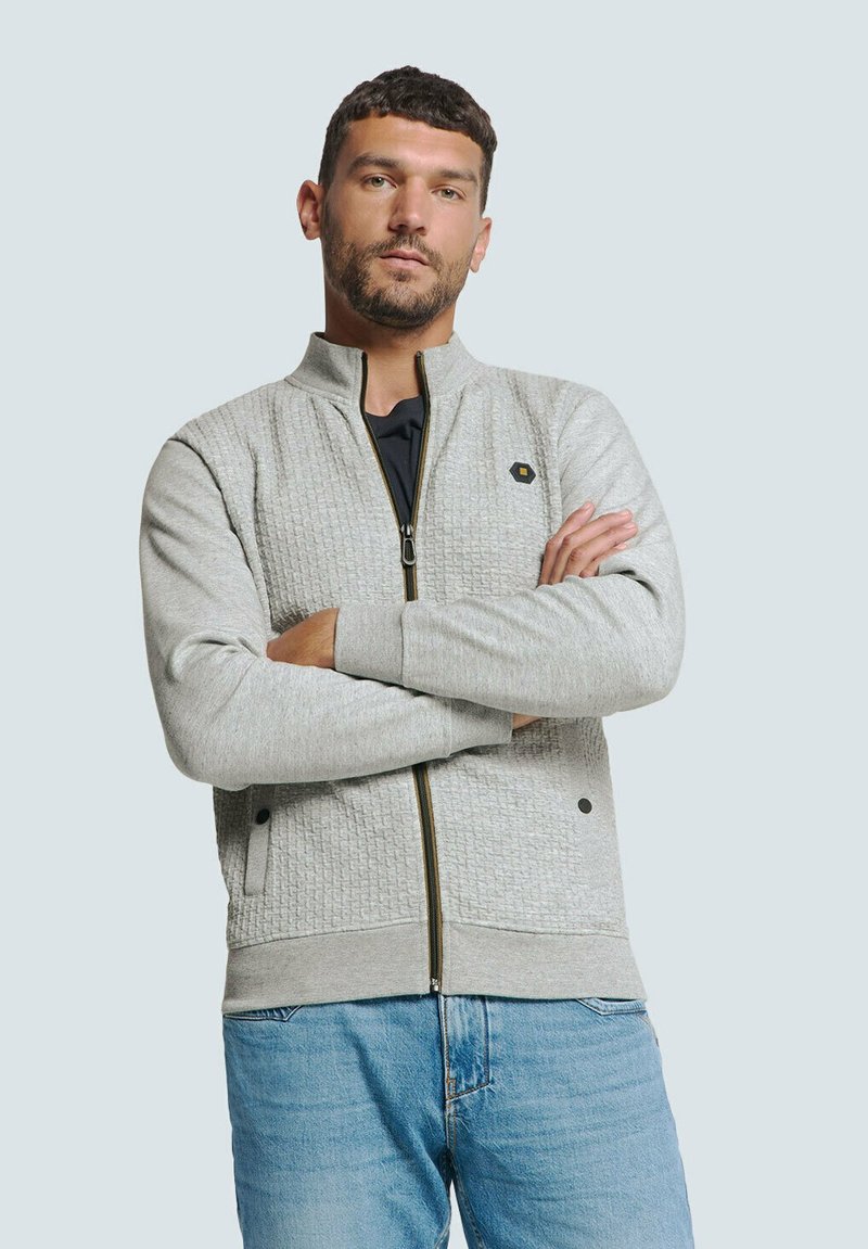 Lichtgrijze zip-up jas met textuurpanelen, zwarte hardware-accenten en geribde boorden. Draag over een donkere top en gecombineerd met lichte denim jeans.