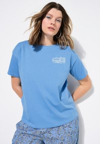 Lichtblauwe katoenen t-shirt met korte mouwen, voorzien van een witte grafische afbeelding op de linkerkant van de borst. Gecombineerd met blauwe broeken met een paisleypatroon.