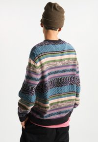 Multicolored knitted sweater featuring blue, green, and purple stripes with textured patterns; ribbed collar and cuffs; layered over a pink shirt.