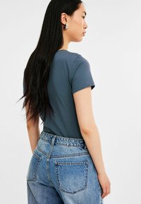 Mörkblå t-shirt med kort ärm, kombinerad med höga ljusblå jeans som har en urblekt textur och stora bakfickor.