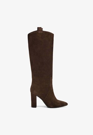 Stivale al ginocchio in suede marrone con punta appuntita, tacco blocco e una linguetta distintiva sul retro per facilitare l'indossamento. Texture liscia su tutta la superficie.