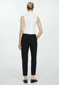 Top blanco sin mangas con un cuello alto, combinado con pantalones ajustados negros. El conjunto presenta líneas limpias y un diseño a medida.