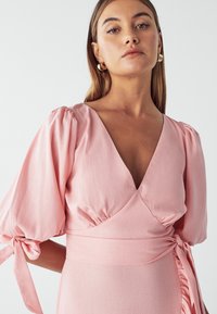 Pink wrap dress with puff sleeves, V-neckline, and tie detail at the waist. Smooth, lightweight fabric with a soft sheen.