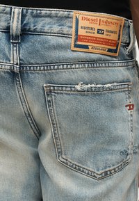 Πίσω όψη ανοιχτό μπλε τζιν με ξεφτισμένες άκρες τσέπης και δερμάτινη ετικέτα Diesel Industry στη μέση.