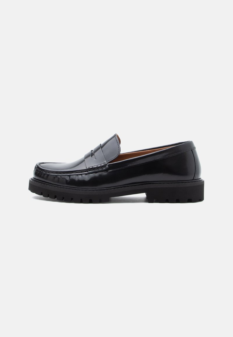 Melna ādas peni loafer kurpe ar masīvu gumijas zoli un moc toe šuvēm, parādīta profilā uz baltas fona.