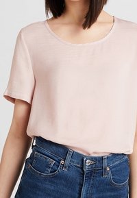 Ljust rosa blus med korta ärmar, rund halsringning och slät tyg. Matchas med mörkblå denimjeans med framfickor.