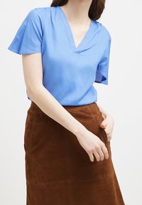 Blusa blu a maniche corte con scollatura a V, in tessuto liscio. Abbinata a una gonna A-line in suede marrone con dettagli di cucitura.