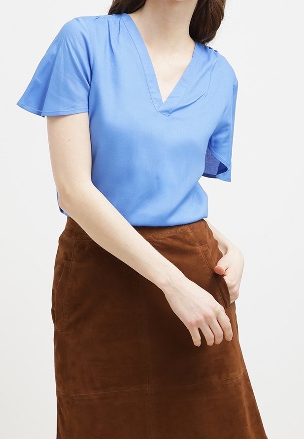 Blusa blu a maniche corte con scollatura a V, in tessuto liscio. Abbinata a una gonna A-line in suede marrone con dettagli di cucitura.