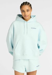 Conjunto de sudadera con capucha y pantalones cortos en azul claro, hecho de tela suave. La sudadera presenta un bolsillo frontal y capucha con cordón; los pantalones cortos son simples y a juego.