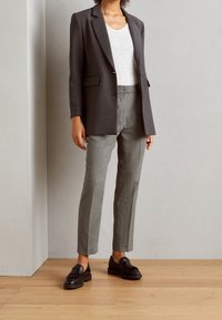 Blazer gris tailleur porté sur une chemise blanche, assorti à un pantalon à motif pied-de-poule et des mocassins noirs. Couleur unie et design structuré.