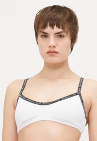 Bralette bianco con spalline nere con logo; presenta una texture liscia e un design triangolare; spalline regolabili per una vestibilità ottimale.